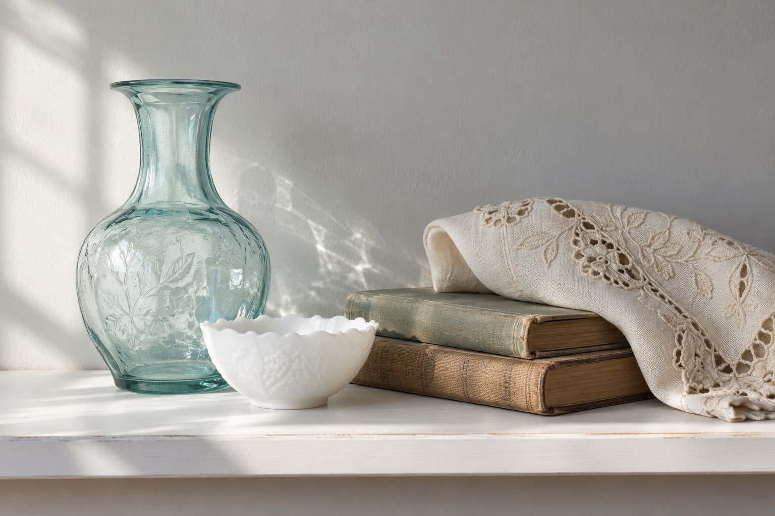 Illustrative vintage glass vase, milk-glass bowl, old books and embroidered textile on a shelf